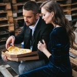 Side view of stylish couple with italian cheese pizza resting on street