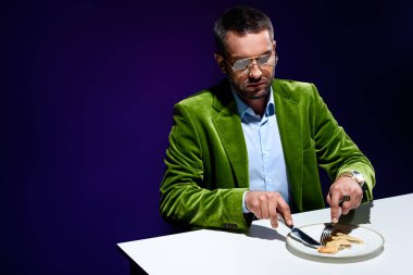 arka plan mavi tabakta et pasta ile masada oturan şık yeşil kadife ceketli adamı portresi