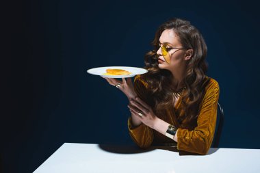 sağlıksız et pasta plaka arkasında mavi arka plan ile masada oturan ile şık giyim güzel kadın