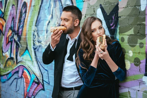 Portrait Couple Vêtements Luxe Mangeant Des Hot Dogs Près Mur — Photo