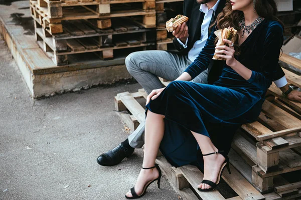 通りに木製のパレットの上に座ってホットドッグと豪華な服でカップルのショットをトリミング — ストック写真