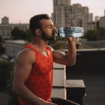 Vue latérale du beau sportif buvant de l'eau sur le toit