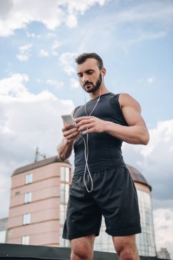 müzik dinleme ve çatıda smartphone kullanarak yakışıklı sporcu düşük açılı görünümü