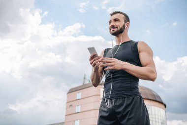 neşeli sporcu dinleme müzik smartphone ve uzak çatıda arıyorsunuz düşük açılı görünüş 