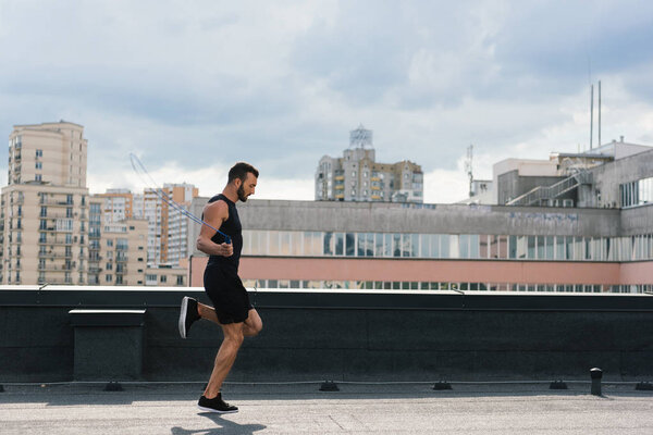 side view of handsome sportsman jumping with jumping rope on roof