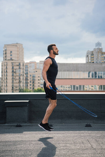 side view of handsome sportsman training with jumping rope on roof