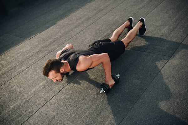 high angle view of handsome sportsman doing push ups with dumbbells on roof