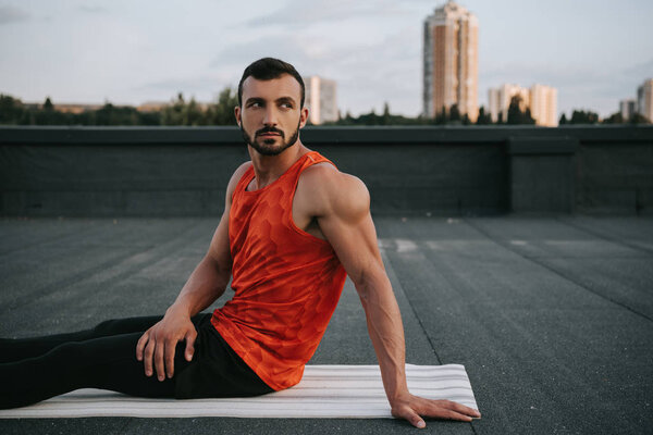 красивый мужчина отдыхает на коврике для йоги после занятий йогой на крыше
