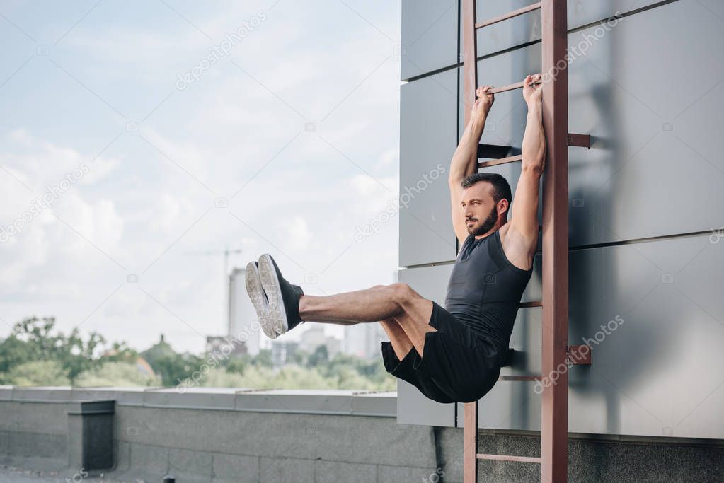 Handsome sportsman doing leg raises on ladder on roof