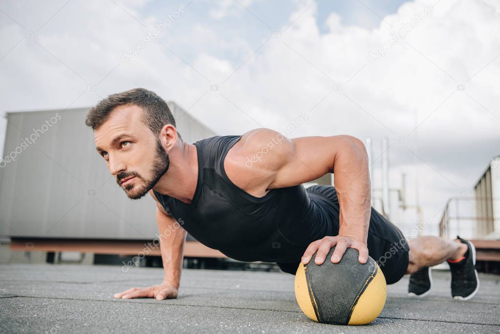 handsome sportsman doing push ups with medicine ball on roof