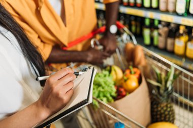 Kadının arabası süpermarkette alışveriş ile yakın duran erkek arkadaşı ise alışveriş listesi işaretleme kırpılmış görüntü