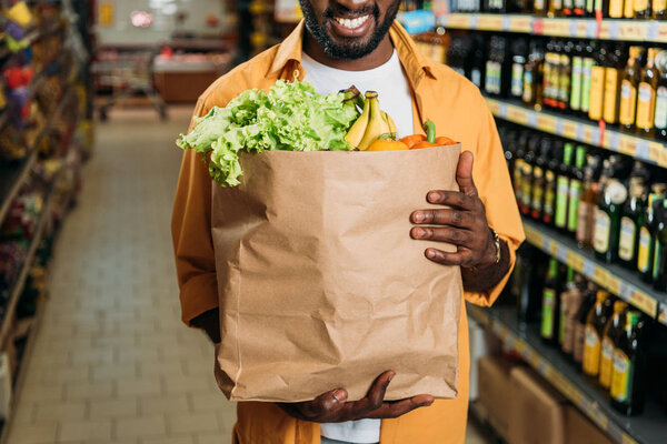 cropped image of african american man holding paper bag with food in grocery store