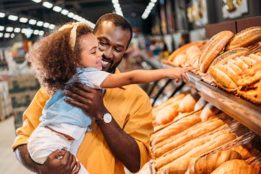 african american little child pointing by finger at pastry to father in supermarket  clipart