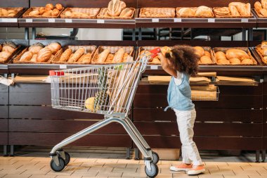 süpermarkette alışveriş arabası taşıyan küçük Afro-Amerikan çocuk yan görünüm