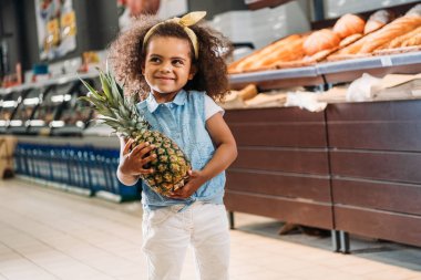 Süpermarkette ananas ile ayakta gülümseyen Afro-Amerikan çocuk 