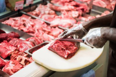 partial view of african american male shop assistant cutting steak of raw meat in supermarket  clipart