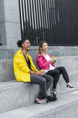 gülümseyen genç çok ırklı çift kentsel Sokağı'nda hamburger yemek