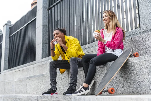 Jovem Casal Multicultural Skatistas Comendo Hambúrgueres Rua Cidade — Fotografia de Stock