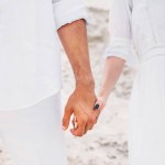 Schnappschuss eines Paares in weißen Kleidern, das Händchen haltend vor einer Sanddüne steht