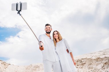 happy young couple taking selfie with monopod and smartphone in desert clipart