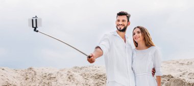 Selfie monopod ve smartphone ile çölde alarak gülümseyen genç çift