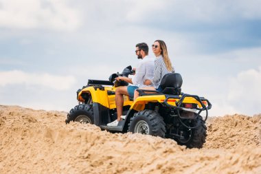 active young couple riding all-terrain vehicle in desert on cloudy day clipart