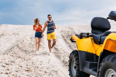 relaxed young couple with atv and coconut cocktails in desert on cloudy day clipart