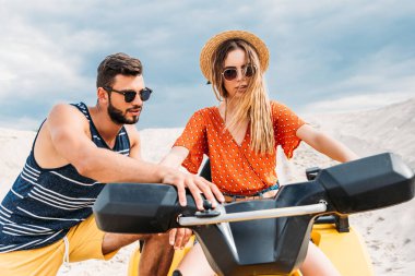 handsome young man teaching his girlfriend how to ride atv in desert clipart