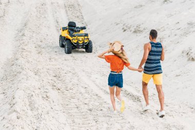 rear view of young couple going to ATV by sandy dune clipart