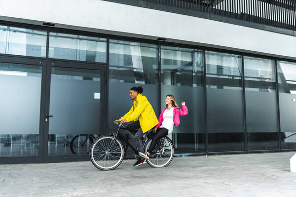 счастливая мультикультурная пара на велосипеде на городской улице
