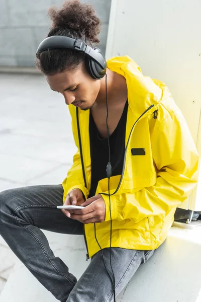 在城市街道上使用智能手机的耳机收听音乐的混合种族男子选择焦点 — 免费的图库照片