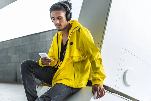 时尚混合的男子在耳机听音乐与智能手机在城市街 — 免费的图库照片