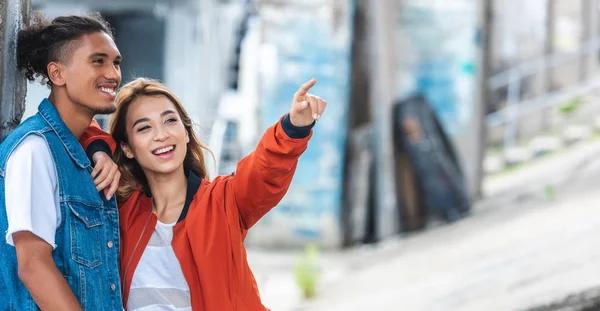 有选择的焦点微笑的亚洲妇女手指指向混合的种族男朋友在城市街道 — 图库照片