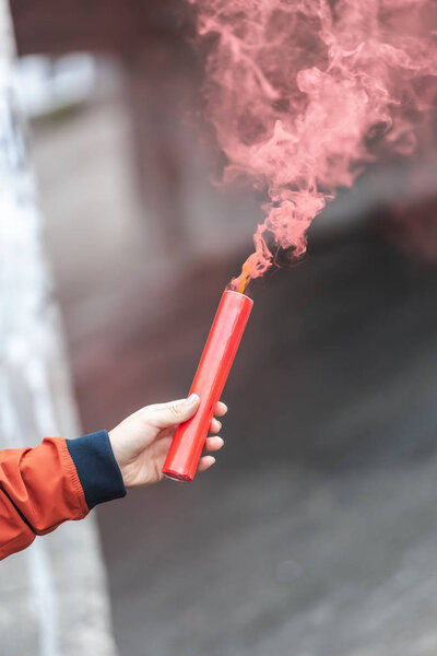 обрезанное изображение молодой женщины, держащей красную дымовую бомбу на городской улице
