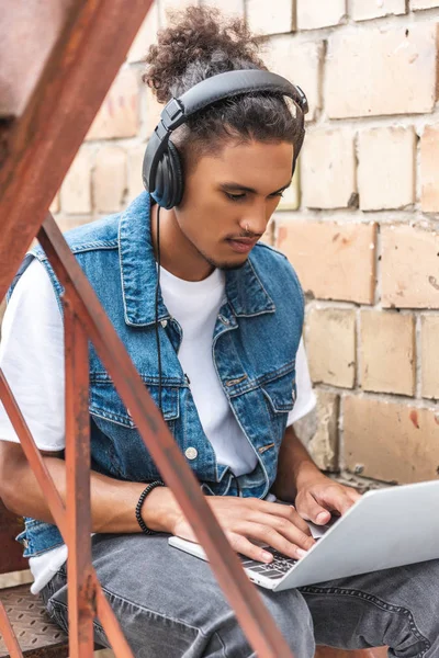 聚焦混合种族男性自由职业者在耳机工作与笔记本电脑在街上 — 图库照片