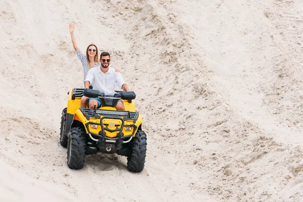 幸せな若いカップル砂漠のバギーに乗って カメラに手を振って — ストック写真