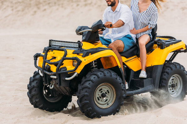 cropped shot of active young couple riding all-terrain vehicle in desert