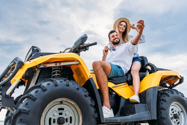 happy young couple sitting on ATV and taking selfie
