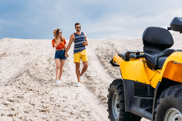 relaxed young couple with atv and coconut cocktails in desert on cloudy day