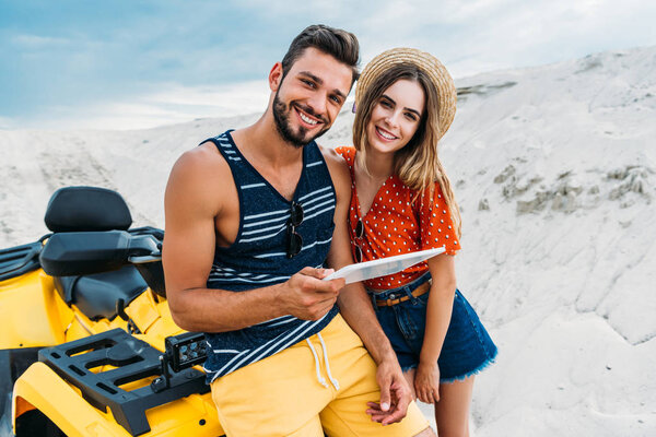 happy young couple with ATV using digital tablet in desert and looking at camera