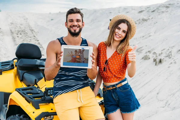 デジタル タブレットの画面と親指に Couchsurfing のウェブサイトを砂漠に現れる Atv と美しい若いカップル — ストック写真