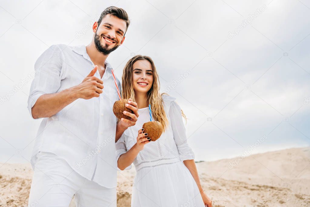 happy young couple in white with coconut cocktails looking at camera