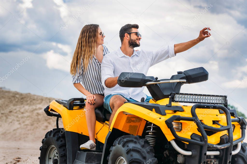 active young couple taking selfie while sitting on ATV in desert