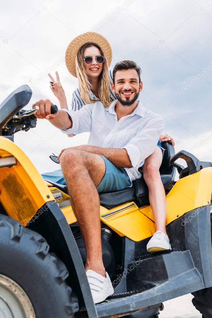 happy young couple sitting on ATV and looking at camera
