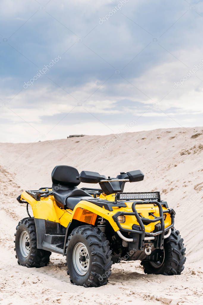 modern yellow all-terrain vehicle standing in desert on cloudy day