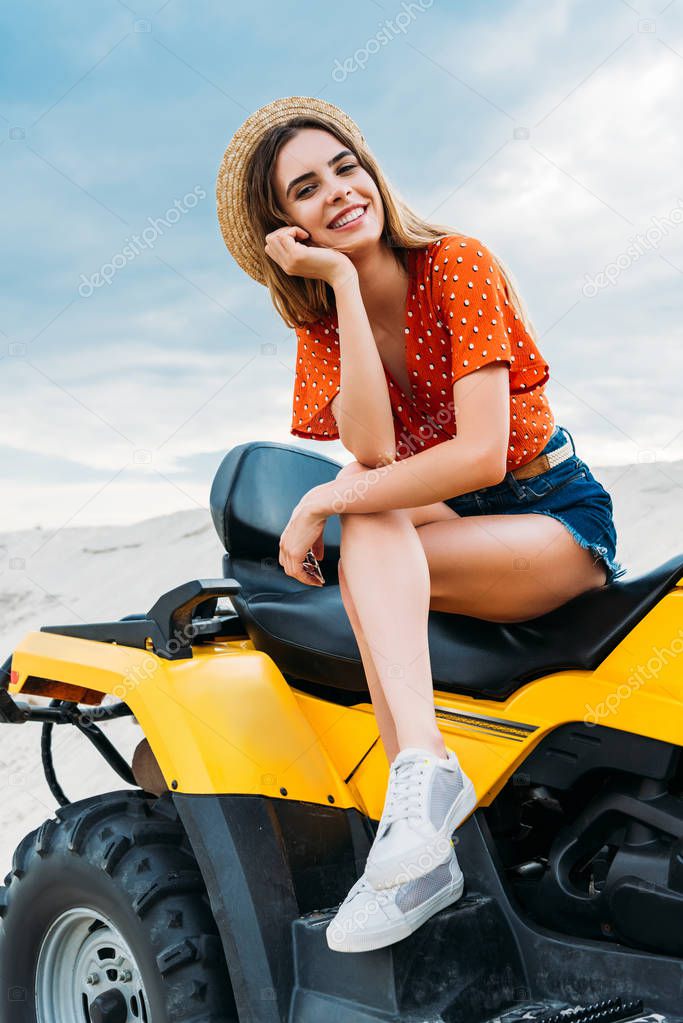 happy young woman sitting on all-terrain vehicle and looking at camera