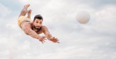 pohledný mladý muž skákání pro míč při hraní plážový volejbal před zamračená obloha