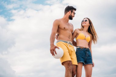 Voleybol topu önünde bulutlu gökyüzü ile mutlu genç çiftin alttan görünüm