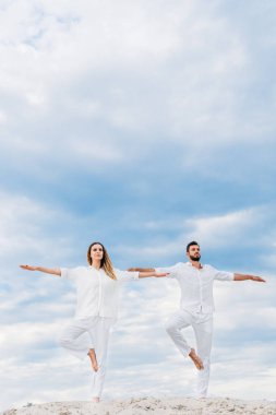 Alt görünümü genç çiftin pratik yoga kabuklarıyla kumlu ağaç poz (Vrksasana)