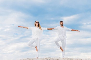 Alt görünümü uygun genç çiftin pratik yoga kabuklarıyla kumlu ağaç poz (Vrksasana)